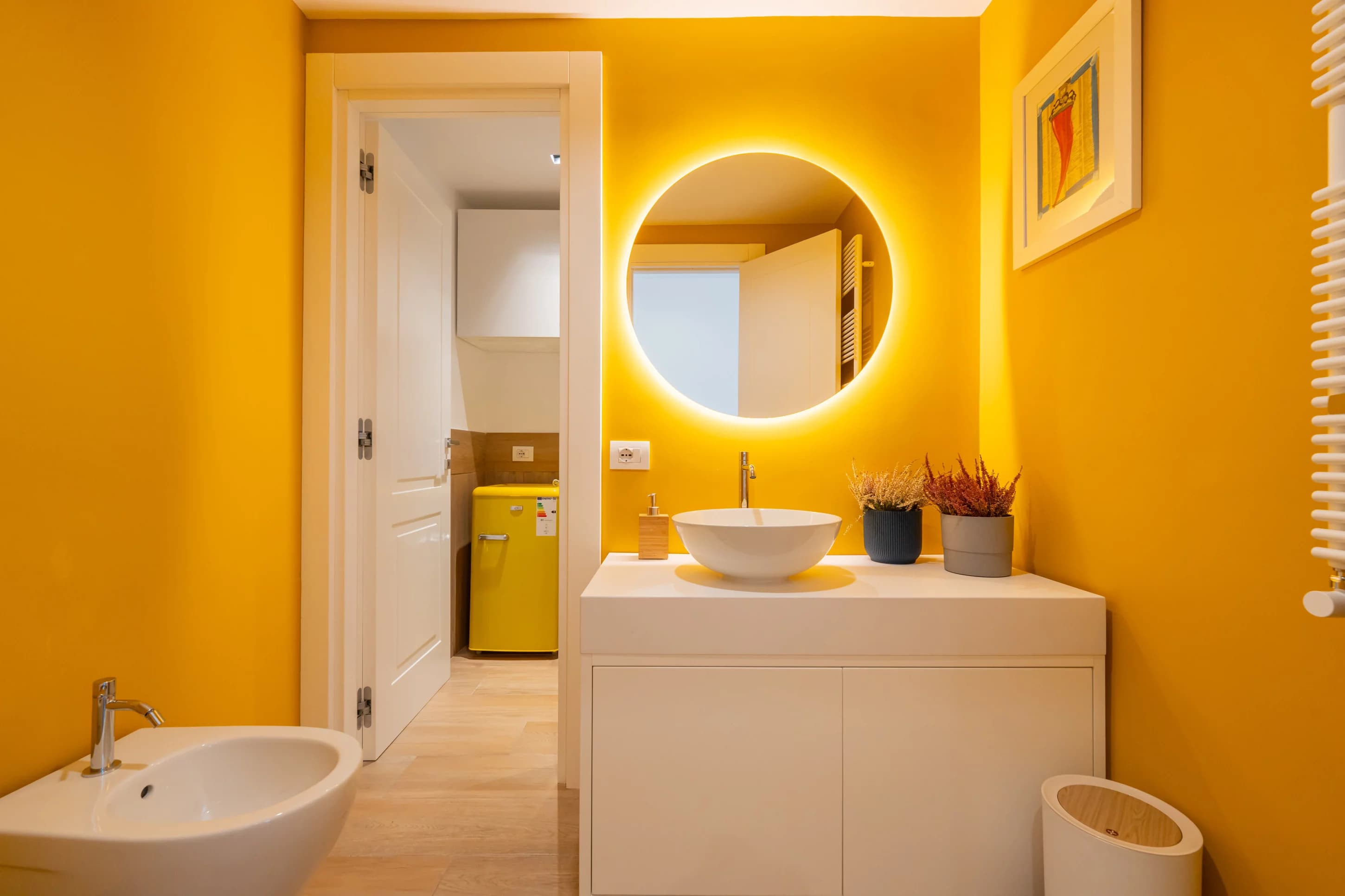 Bagno con pareti gialle, specchio rotondo retroilluminato e lavabo